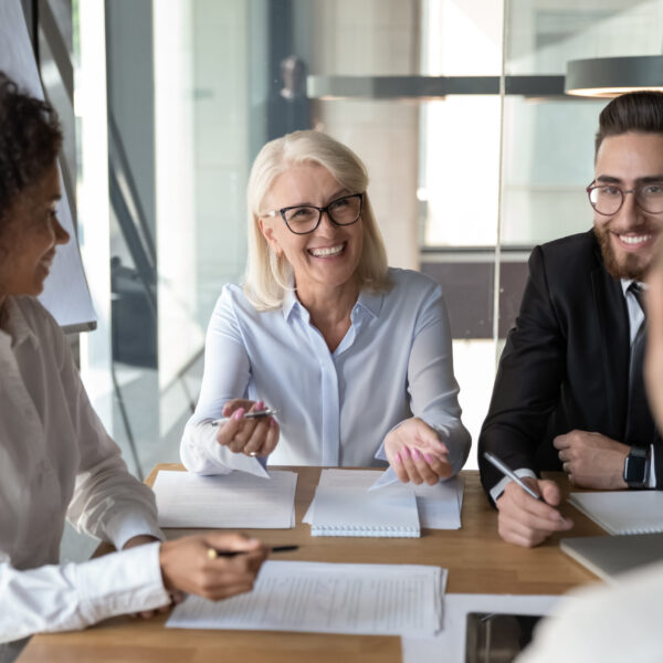 Multi-ethnic office workers chatting at briefing sit at desk in boardroom, different age and ethnicity business partners negotiating during business meeting concept of partnership, friendly relations